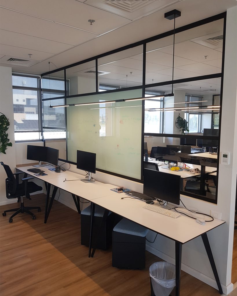 שורת עמדות עבודה עם תאורת פרופילים מינימליסטית ומחיצה זכוכית ירקרקה.