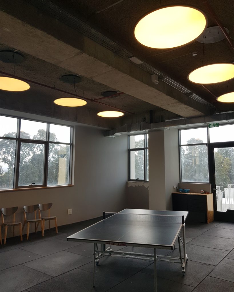 תקרת בטון עם גופי תאורה עגולים גדולים בחלל משחקים עם שולחן פינג פונג.