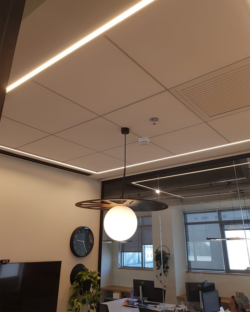 מבט על תקרה אקוסטית עם תאורה שקועה וחפצים תלויים, כולל גוף תאורה כדורי.