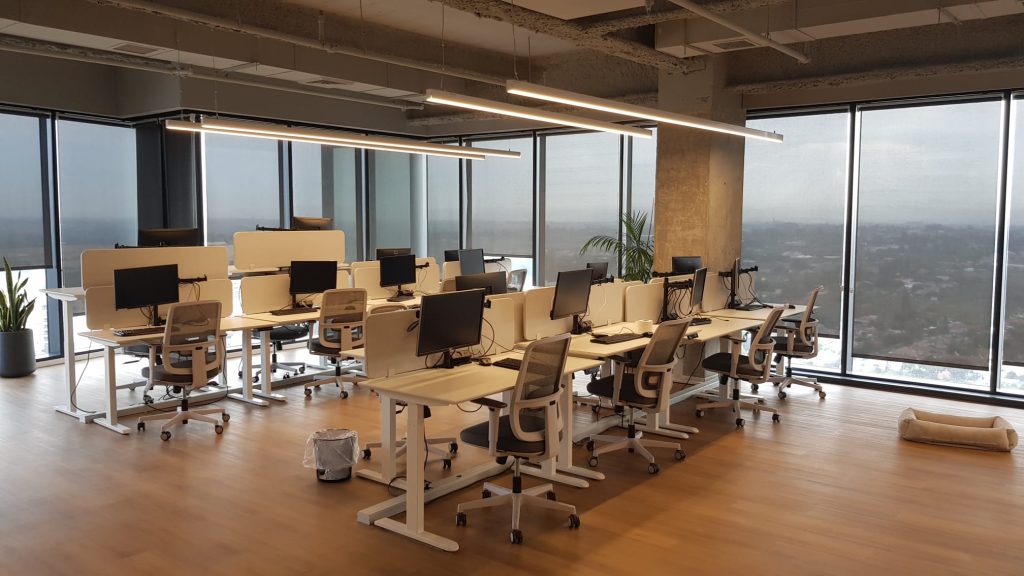 עמדות עבודה מוארות בגופי תאורה ליניאריים תלוים בתקרה תעשייתית חשופה.