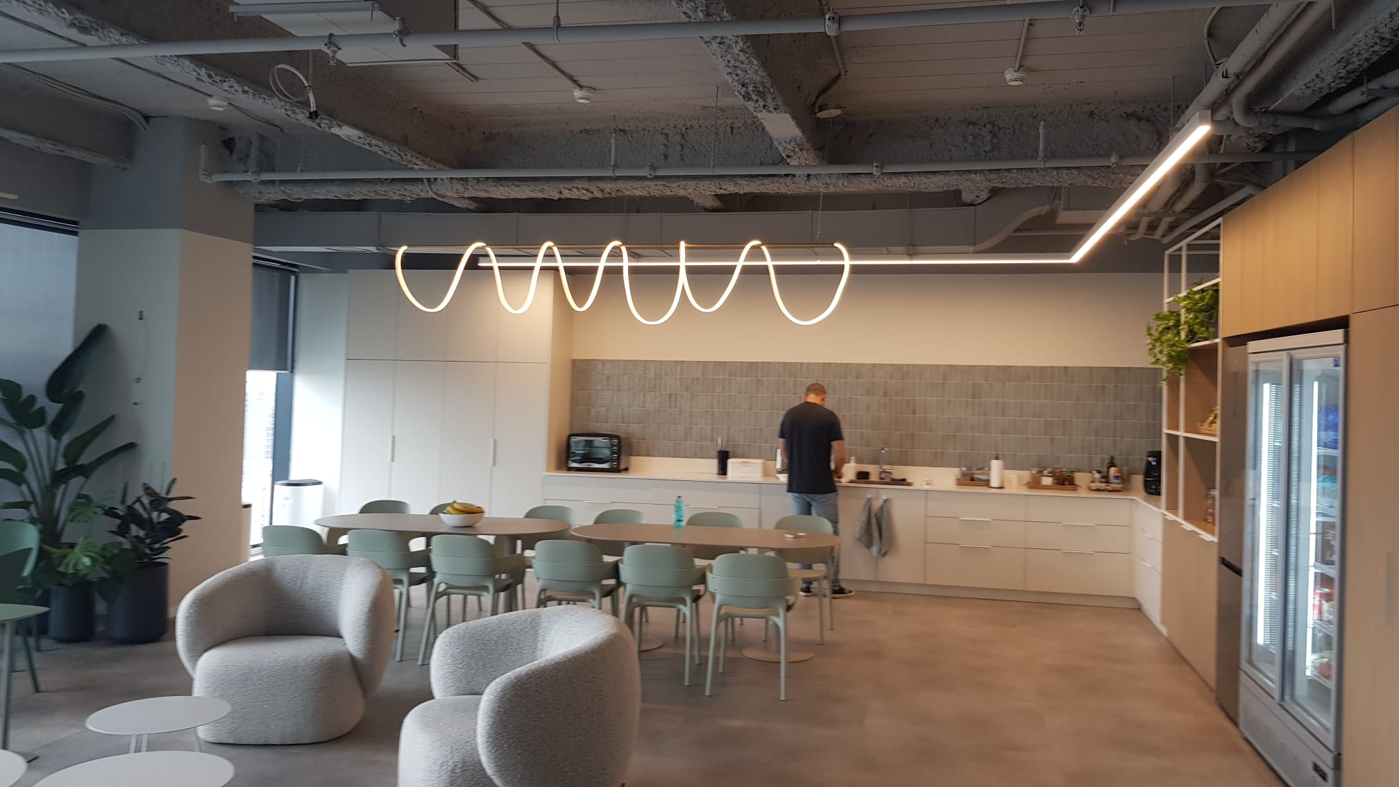 אזור ישיבה מול המטבח, עם תאורה בצורת גלים ומנורות עגולות מעל שולחנות.